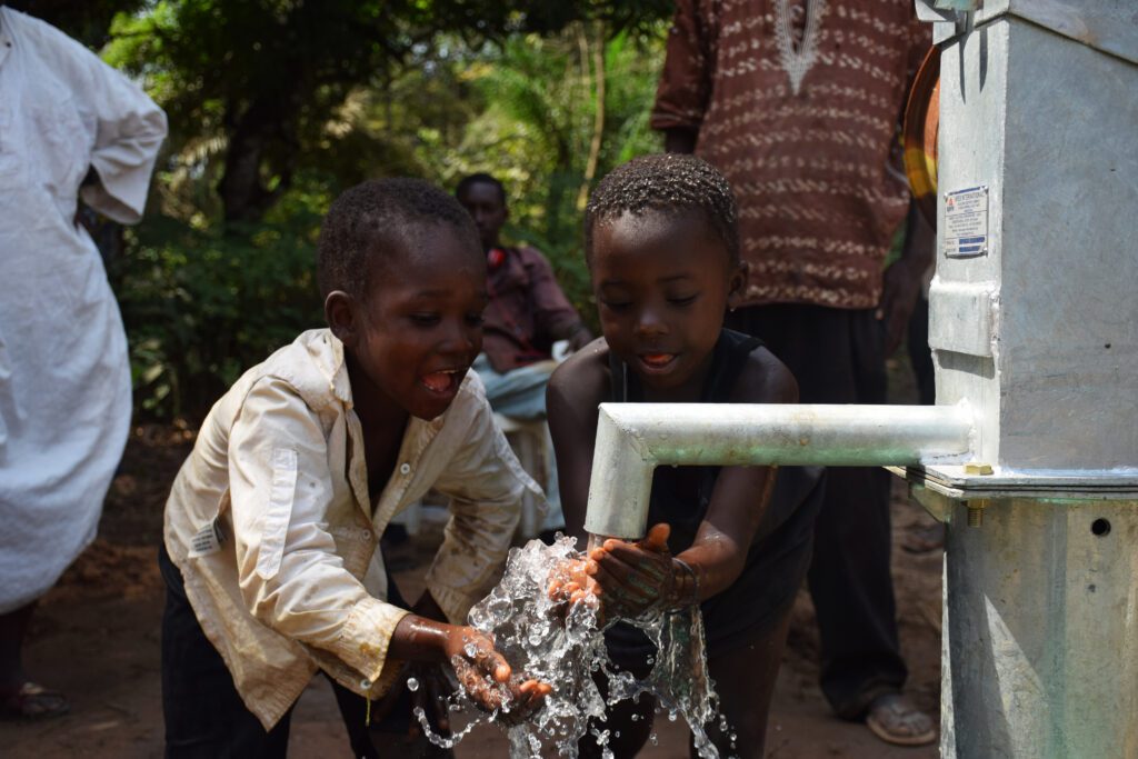 Two young children smiling and touching the water from their village's new well.
